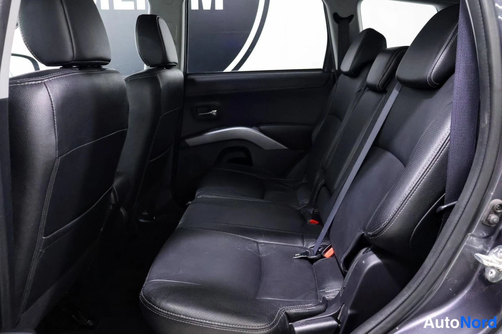 Takaistuimet: Three black leather rear seats with seatbelts mounted on frame side panels and door interior visible