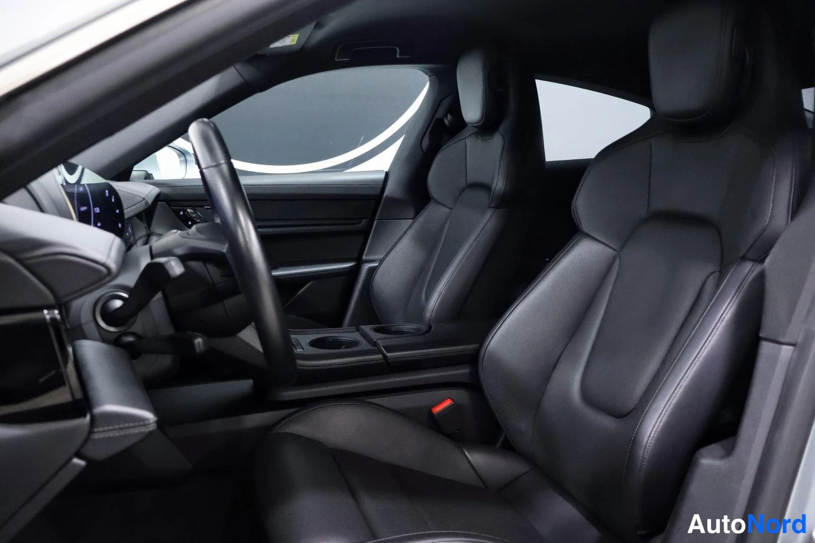 Etuistuimet: Interior view from front passenger side showing black leather front seats, center console with cupholders and steering wheel.