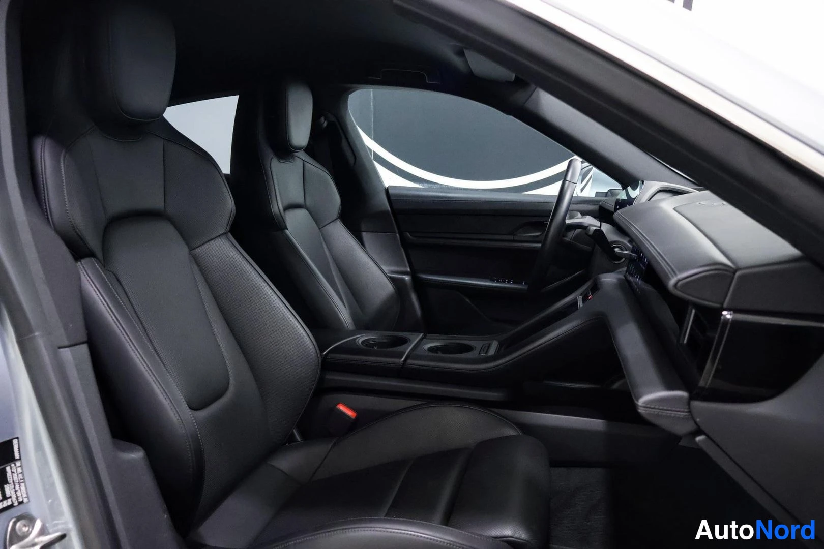 Etuistuimet: Interior view from driver's side looking toward passenger seat, showing two black leather front seats and dashboard area.