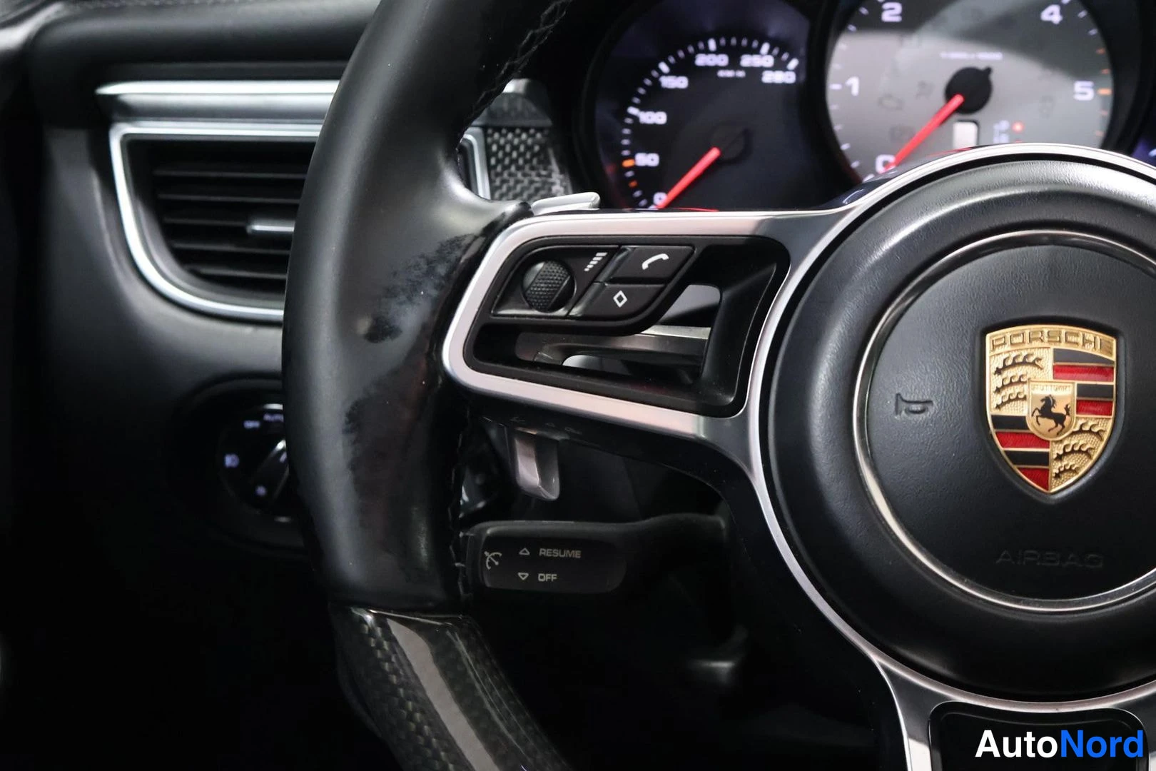 Muu: Ohjauspyörän vasen puolisko ja mittaristo. Ohjauspyörässä Porsche-vaakuna, AIRBAG-teksti ja äänitelefonin/kaukovalon merkkiset painikkeet. Rattiupi nappi RESUME
