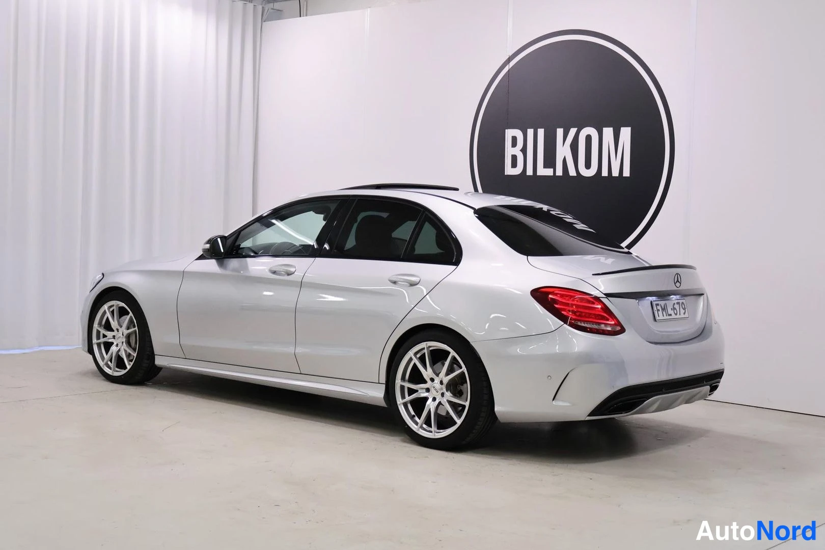Etuviisto, nokka vasemmalle: Silver Mercedes-Benz C-Class photographed from front three-quarter angle showing grille, headlight, driver-side door panel and part of windshield. Pano