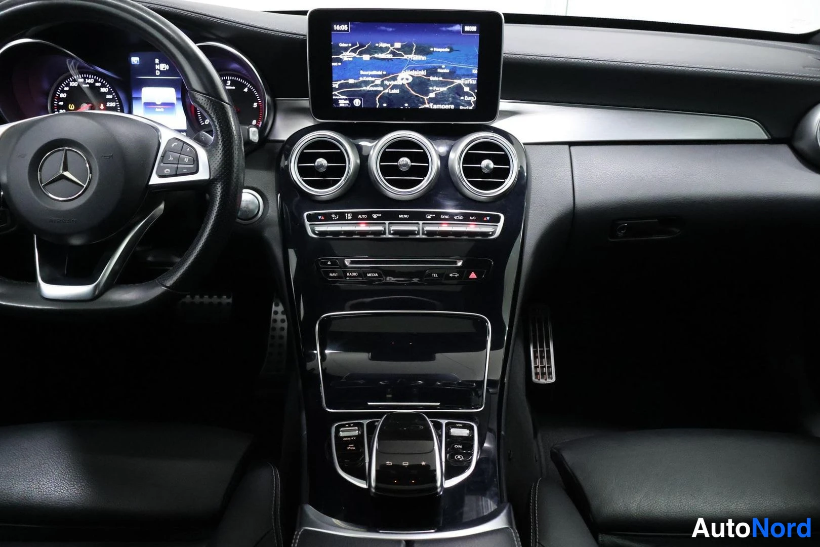 Ohjaamo: Interior view of a vehicle cabin showing the dashboard, three central air vents, infotainment screen displaying a map, steering wheel with buttons and center lo