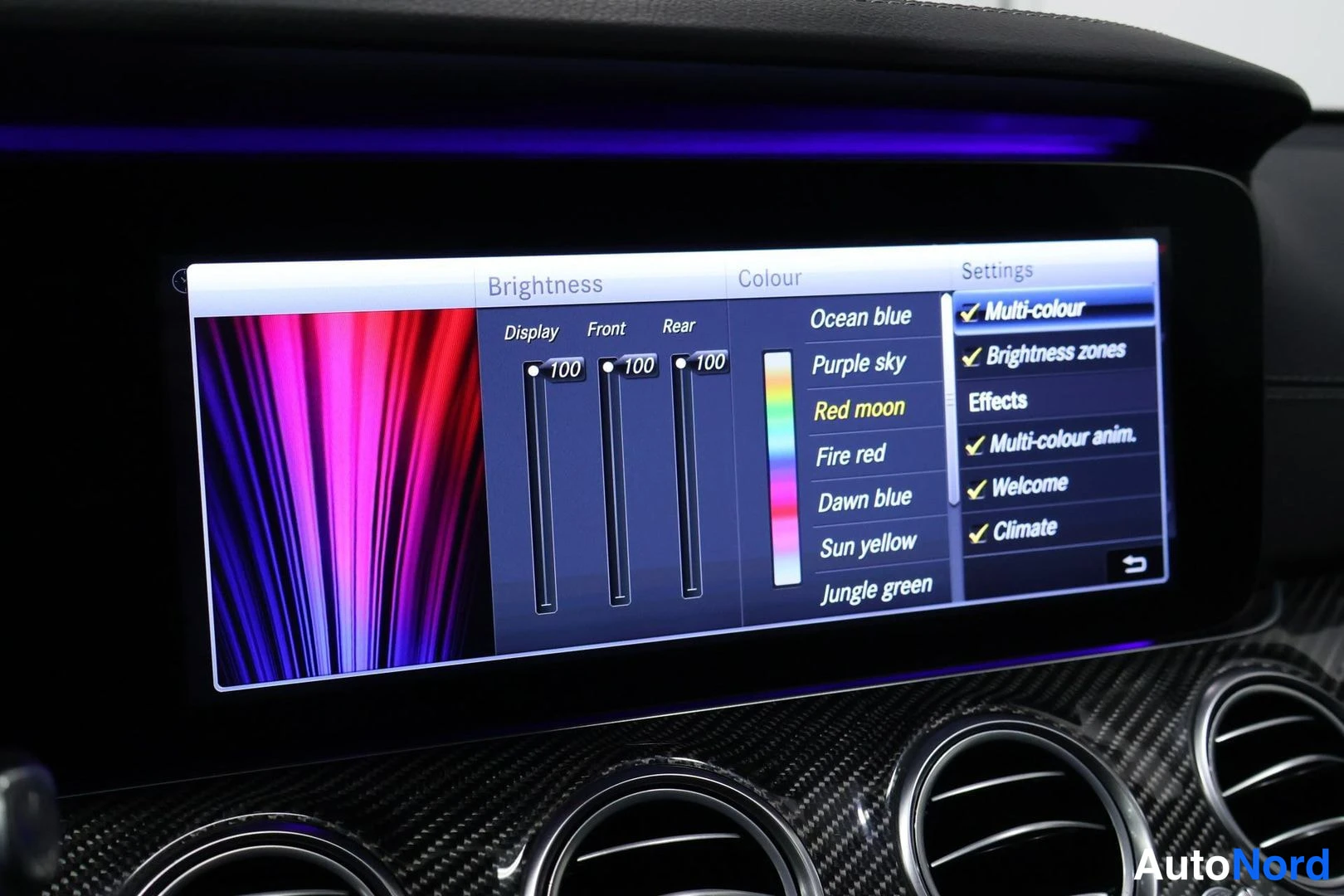 Yksityiskohta: Kojetaulun infotainment-näyttö näyttää ympäristövalaistuksen asetukset: Brightness-säädöt (Display, Front, Rear) arvolla 100, värit kuten Red moon ja Ocean blue