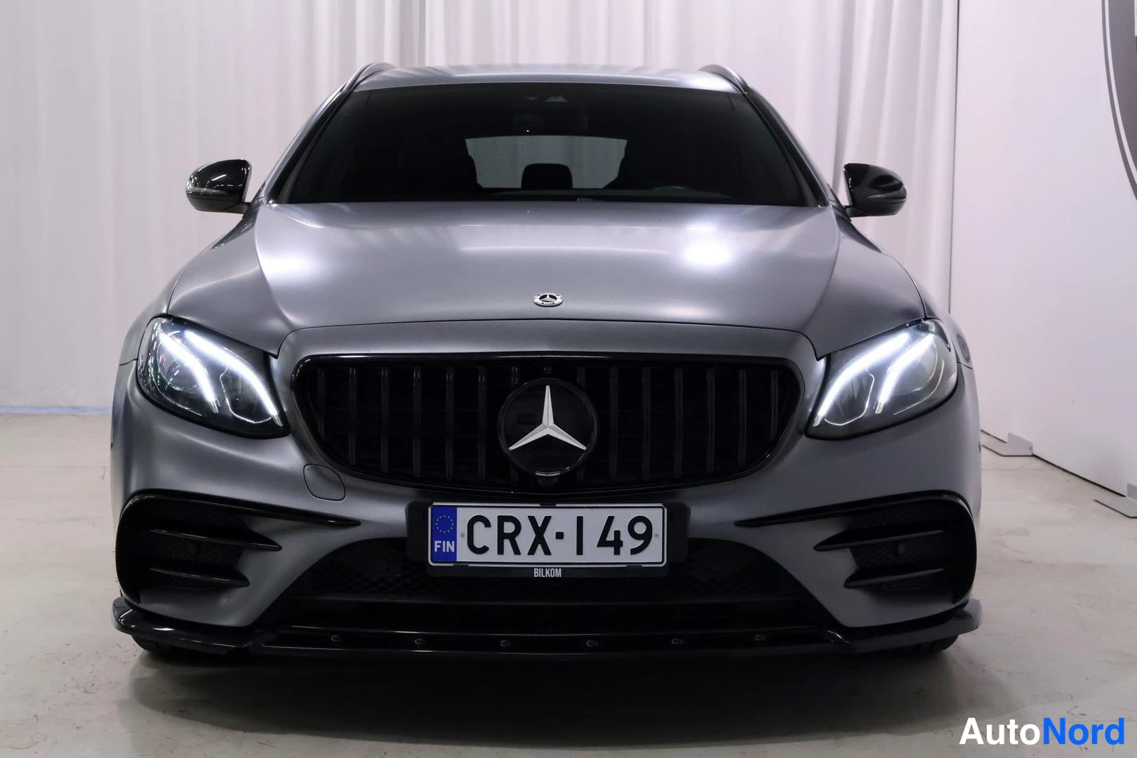 Edestä: Edestä otettu suorakulmainen kuva harmaanvärisen auton edestä, jossa näkyy Mercedes-Benz:n tunnus, LED-taajuiset ajovalot, suuri eturitilä ja rekisterikilpi.