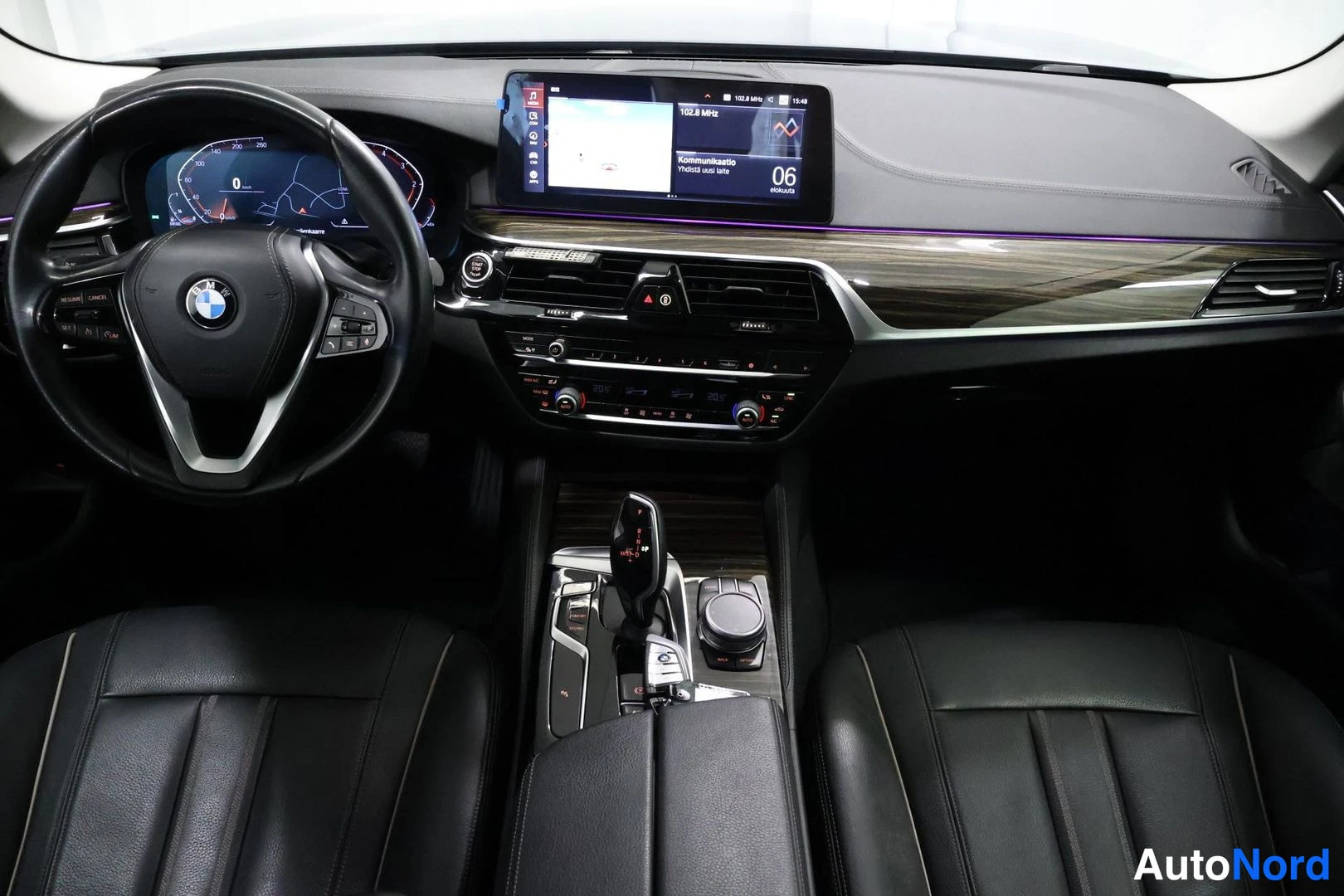 Muu: Kojetaulu ja keskikonsoli edestä: BMW-ohjauspyörä, digitaalinen mittaristo, näyttö keskellä näyttää karttaa ja radiotaajuutta 102.8 MHz, automaattivaihteen vali