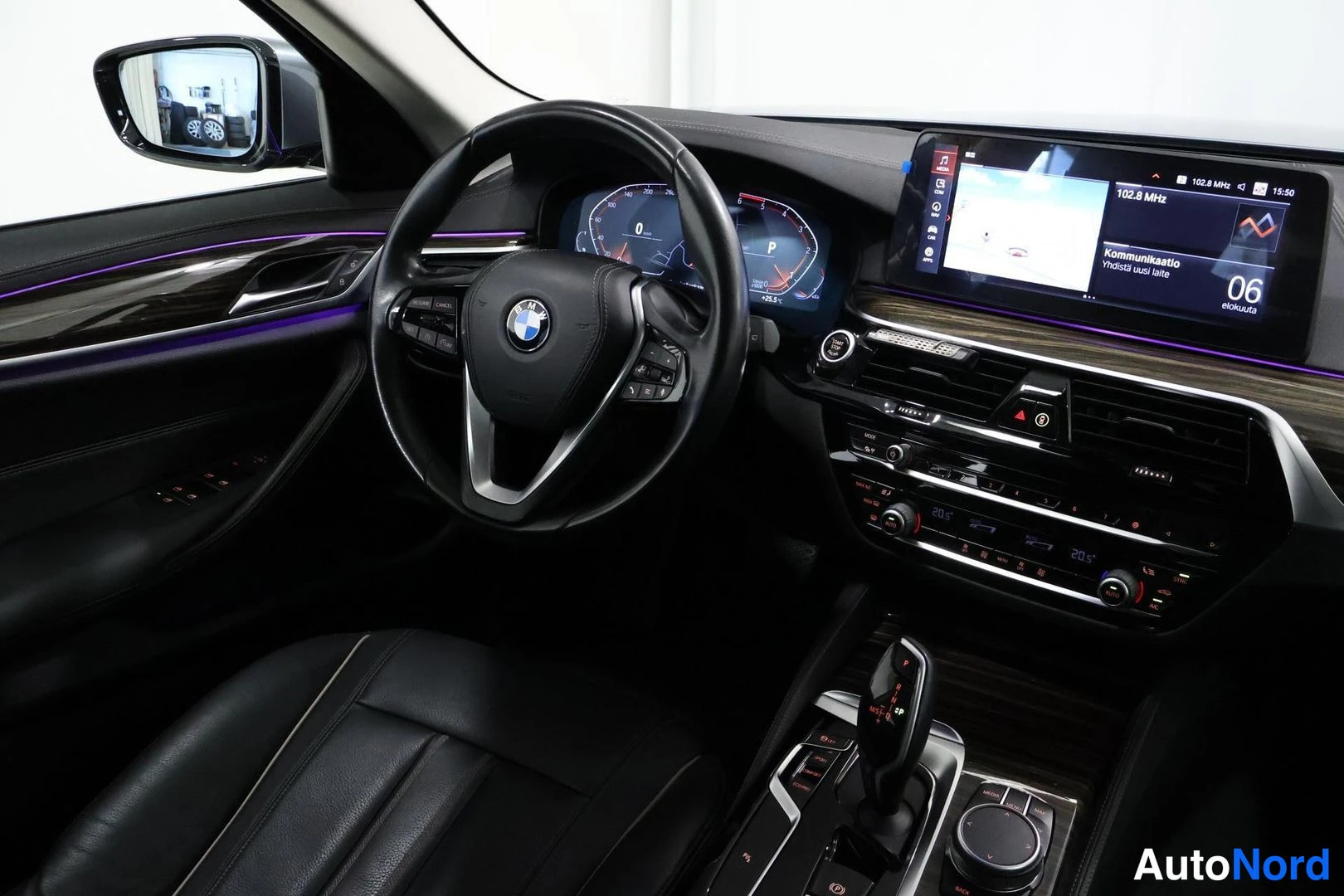 Muu: Kuljettajan puoleinen näkymä kojetauluun: BMW-ohjauspyörä, digitaalinen mittaristo, näyttö kartalla ja viistosti radioilla 102.8 MHz, automaattivaihteiston vali