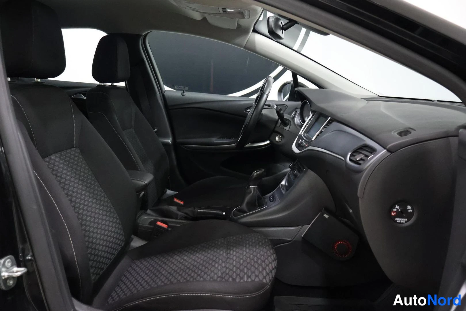 Etuistuimet: Interior cabin view looking from driver's door inward, displaying front seats with patterned inserts, center console with gear lever, and dashboard layout.