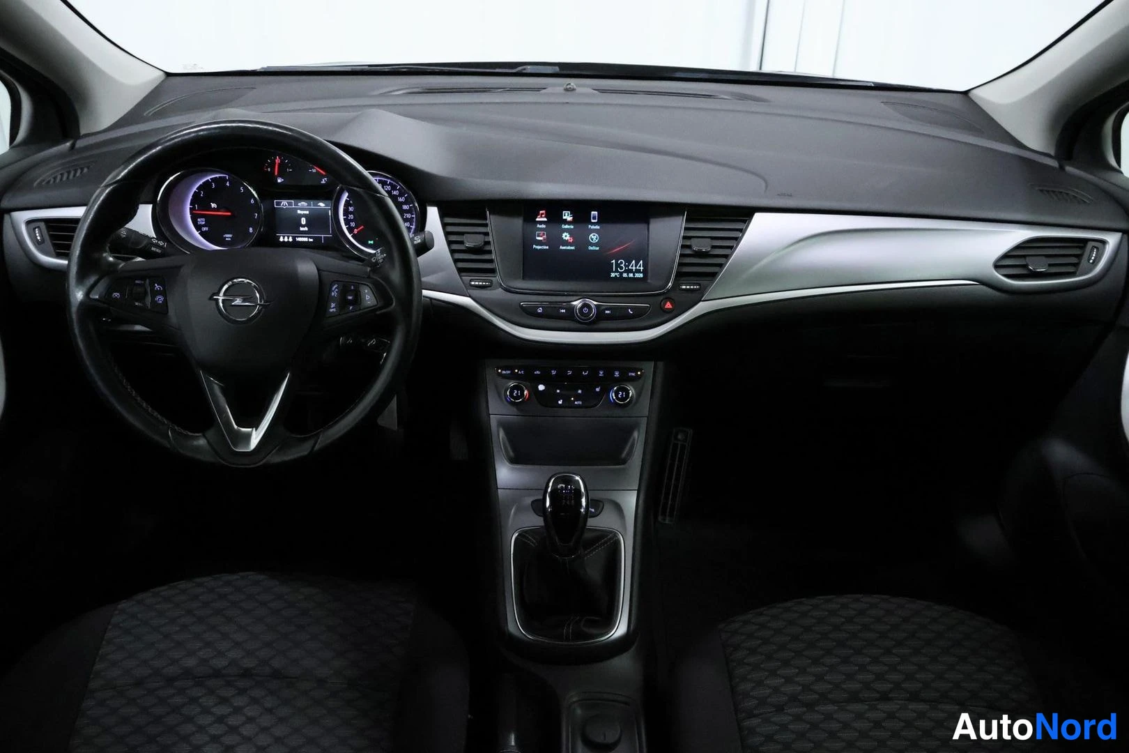 Muu: Kojelaudan ja ohjauspyörän etunäkymä: mallikyltti Opel ohjauspyörässä, infotainment-näyttö, manuaalivaihteiston keila ja tummat kangasistuimet.