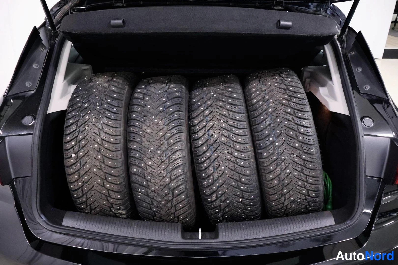 Tavaratila: Open boot of a dark-colored car revealing four winter tires studded and mounted in the cargo area.
