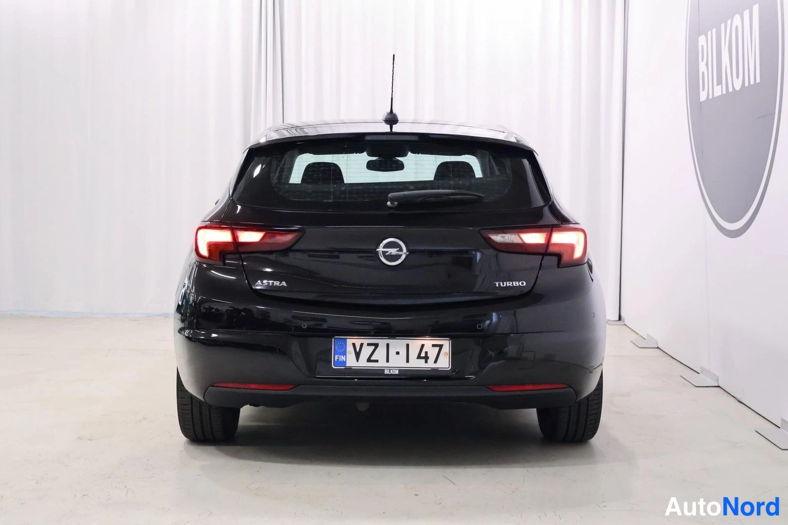 Takaa: Black Opel Astra hatchback viewed from the rear in a studio with white background, showing tail lights, Opel badge, rear wiper, and license plate.