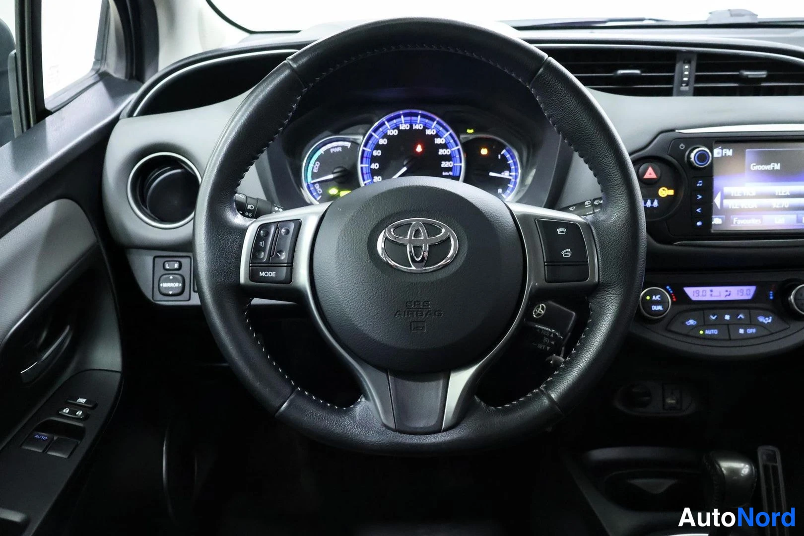 Sivulta: Lähikuva Toyota-ohjauspyörästä, jonka nappaan on painettu SRS AIRBAG -teksti; mittaristo ja kosketusnäyttöradio taustalla.