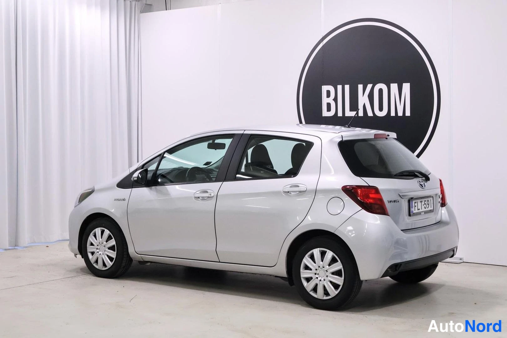 Takaviisto: Hopeanharmaa Toyota Yaris Hybrid takaviistosta oikealta kuvattuna, takana rekisteritunnus.