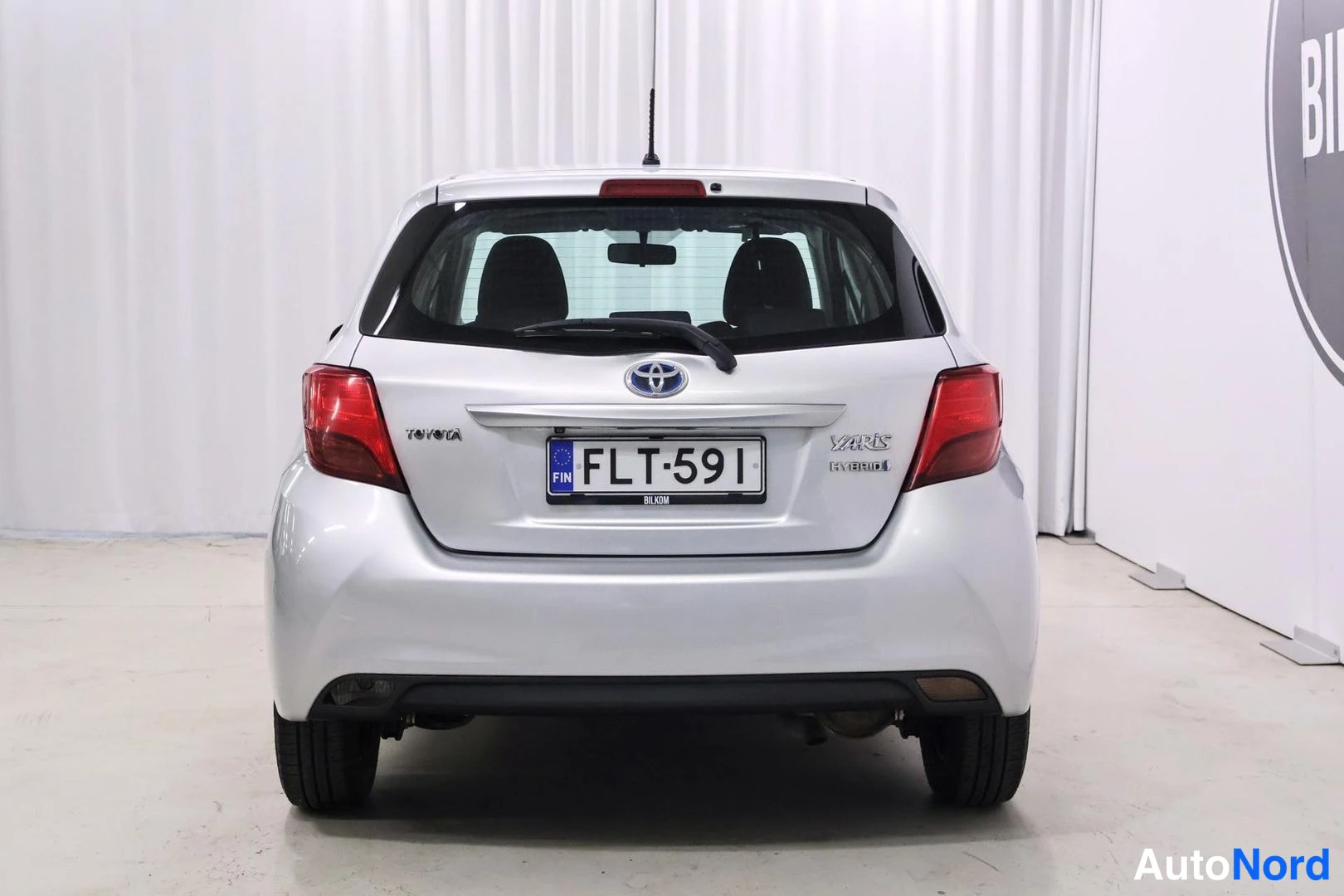 Takaa: Toyota Yaris Hybrid suoraan takaa kuvattuna, rekisteritunnus ja Yaris Hybrid -teksti takaovessa.