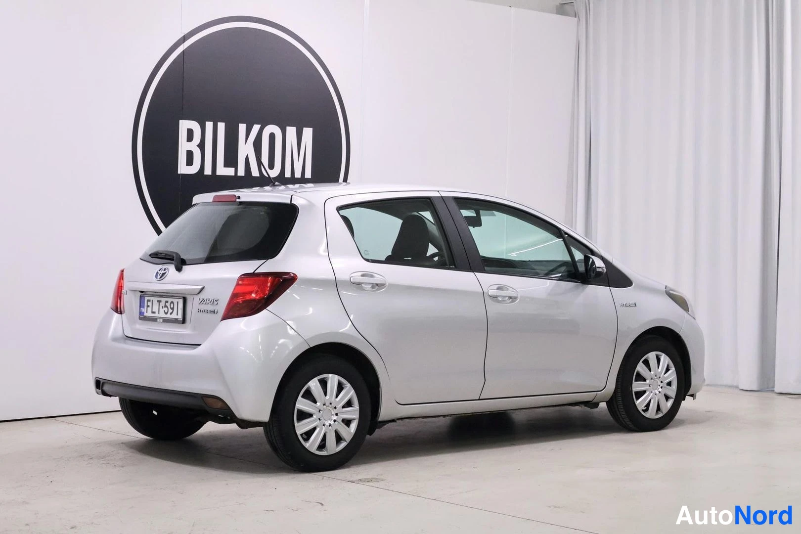 Takaviisto: Hopeanvärinen Toyota Yaris Hybrid kuvattuna takaviistosta; takaluukussa YARIS- ja Hybrid-merkit sekä rekisterikilpi.