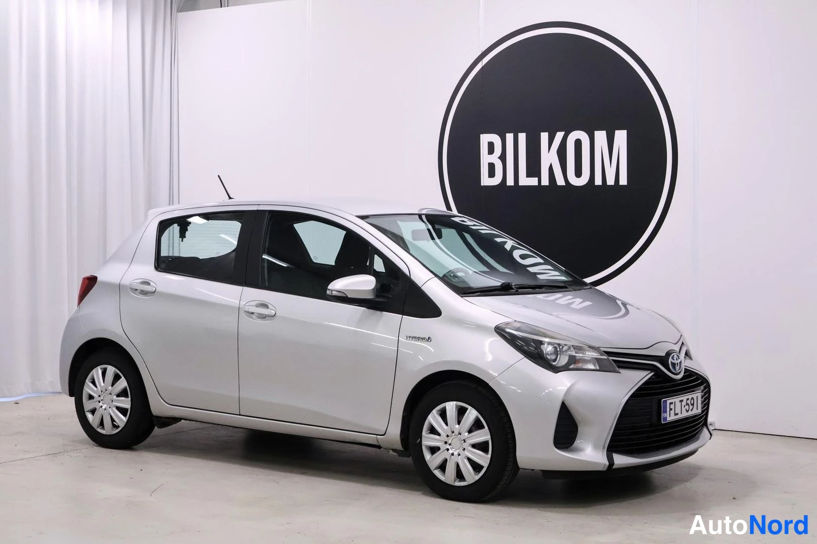 Etuviisto, nokka oikealle: Toyota Yarisin etukulmanäkyva hopeanvärinen viistoperä, rekisterikilpi.