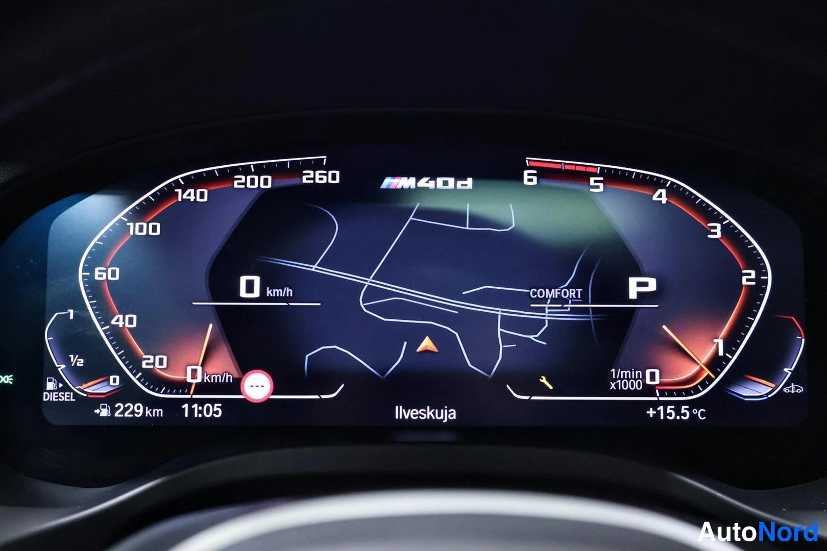 Yksityiskohta: Digitaalinen mittaristo näyttää P-vaihteen, COMFORT-ajotilan, polttoainetiedot (DIESEL, 229 km), kellon 11:05, lämpötilan +15,5 °C ja navigointikartan Ilveskuja