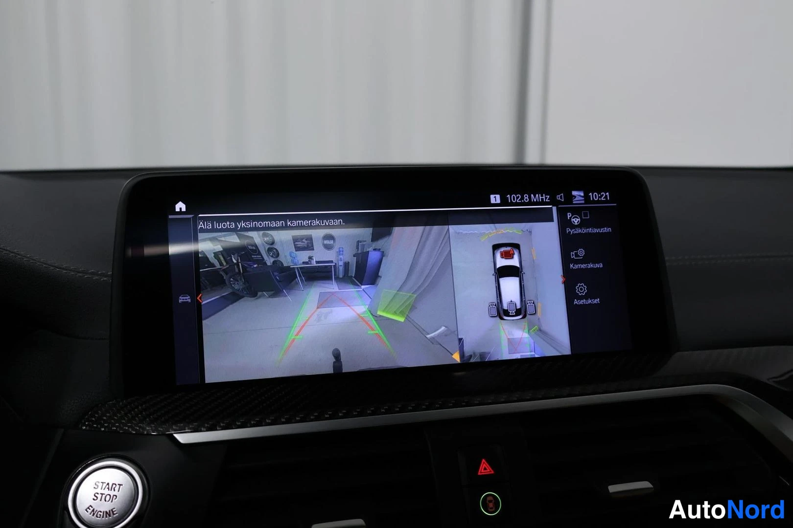 Muu: Auton infotainment-näyttö näyttää peruutuskamerakuvaa ja pysäköintitutkan ympyräpohjaa varoituksella 'Älä luota yksinomaan kamerakuvaan'.