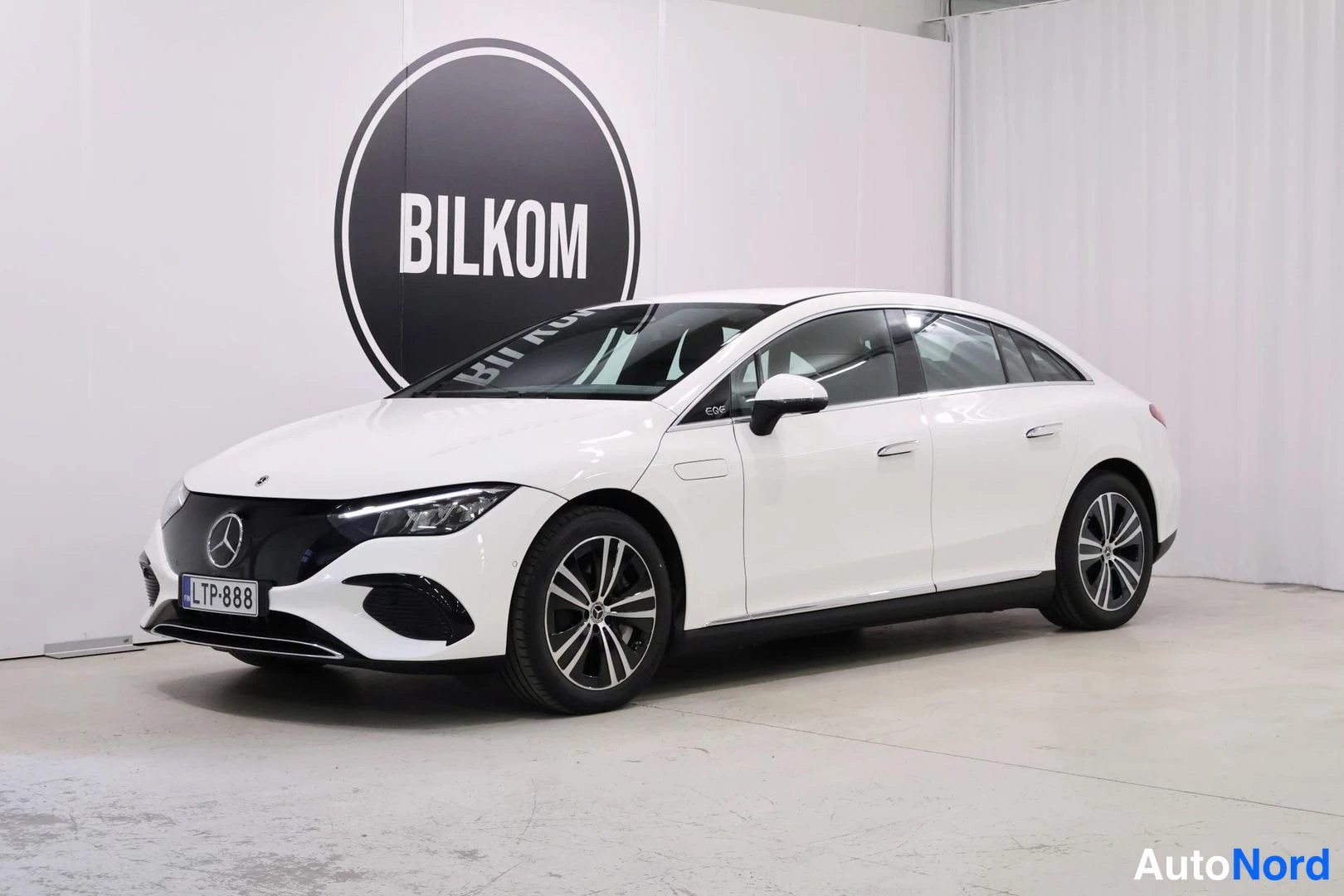 Etuviisto, nokka vasemmalle: Mercedes-Benz EQE -sedani sivulta edestä vasemmalle, valkoinen korimalli, rekisteritunnus.