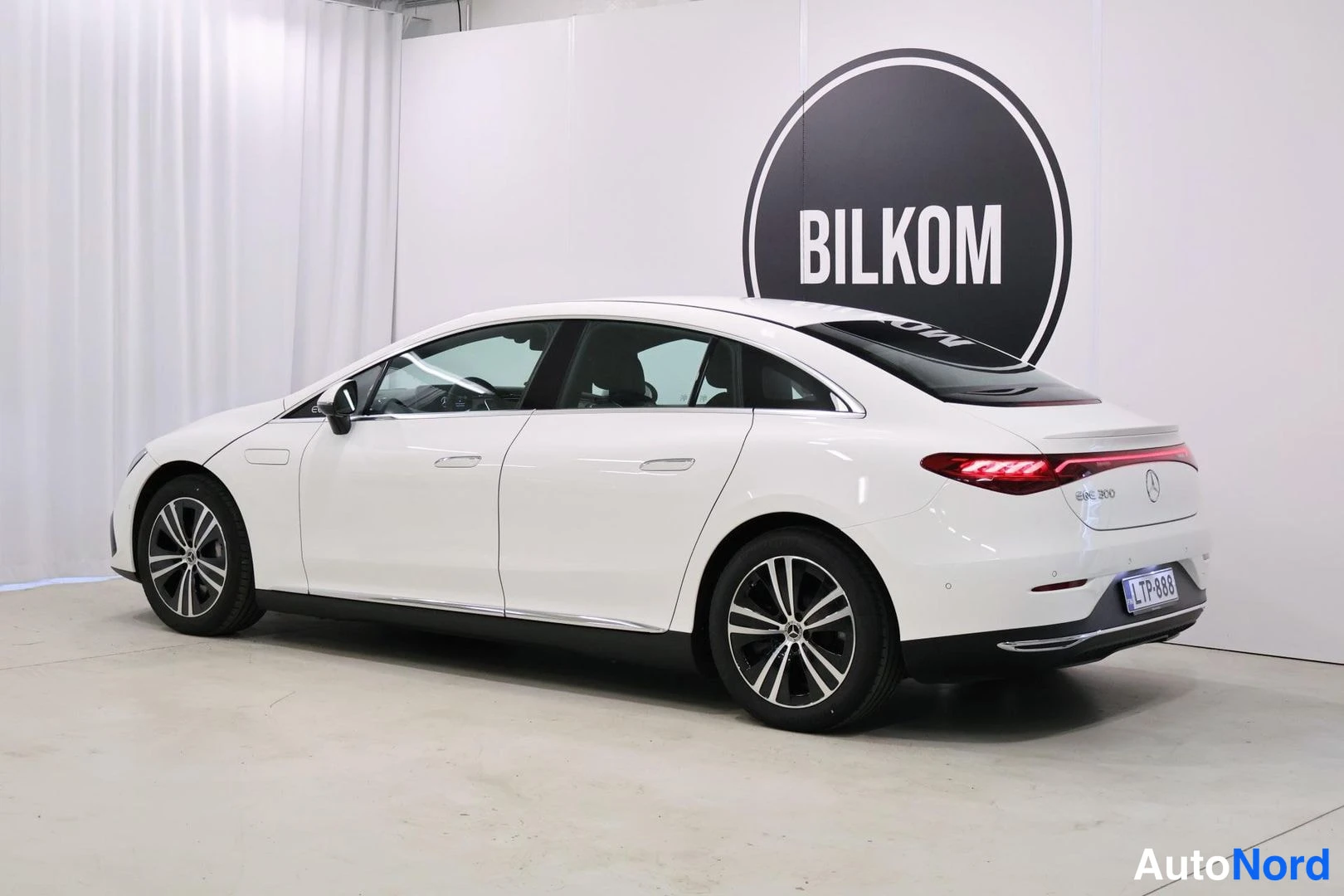 Takaviisto: White sedan from the rear three-quarter angle in a studio
