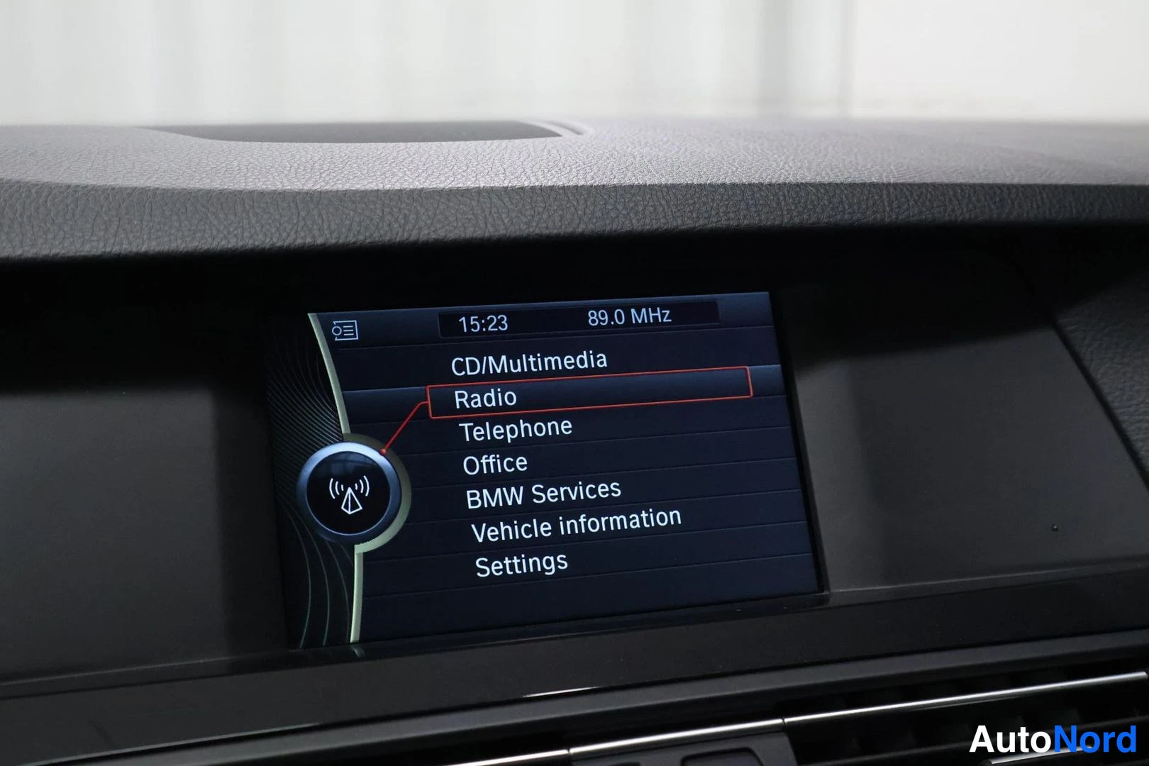 Muu: Kojelaudan näyttö, jossa valikko: CD/Multimedia, Radio, Telephone, Office, BMW Services, Vehicle information, Settings. Kellonaika 15:23 ja taajuus 89.0 MHz.