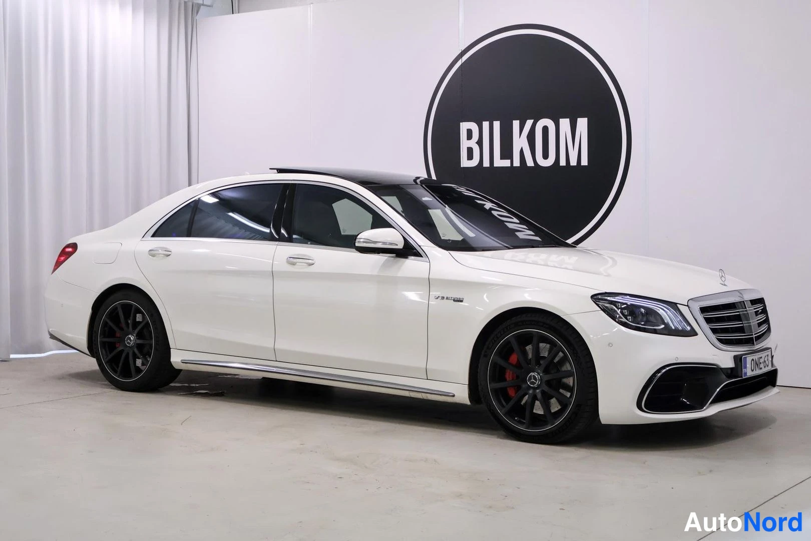 Etuviisto, nokka oikealle: Mercedes-Benz S 63 etukulma oikealla, valkoinen sedan mustilla pulteilla, taivas katsottavissa panoraamakatto