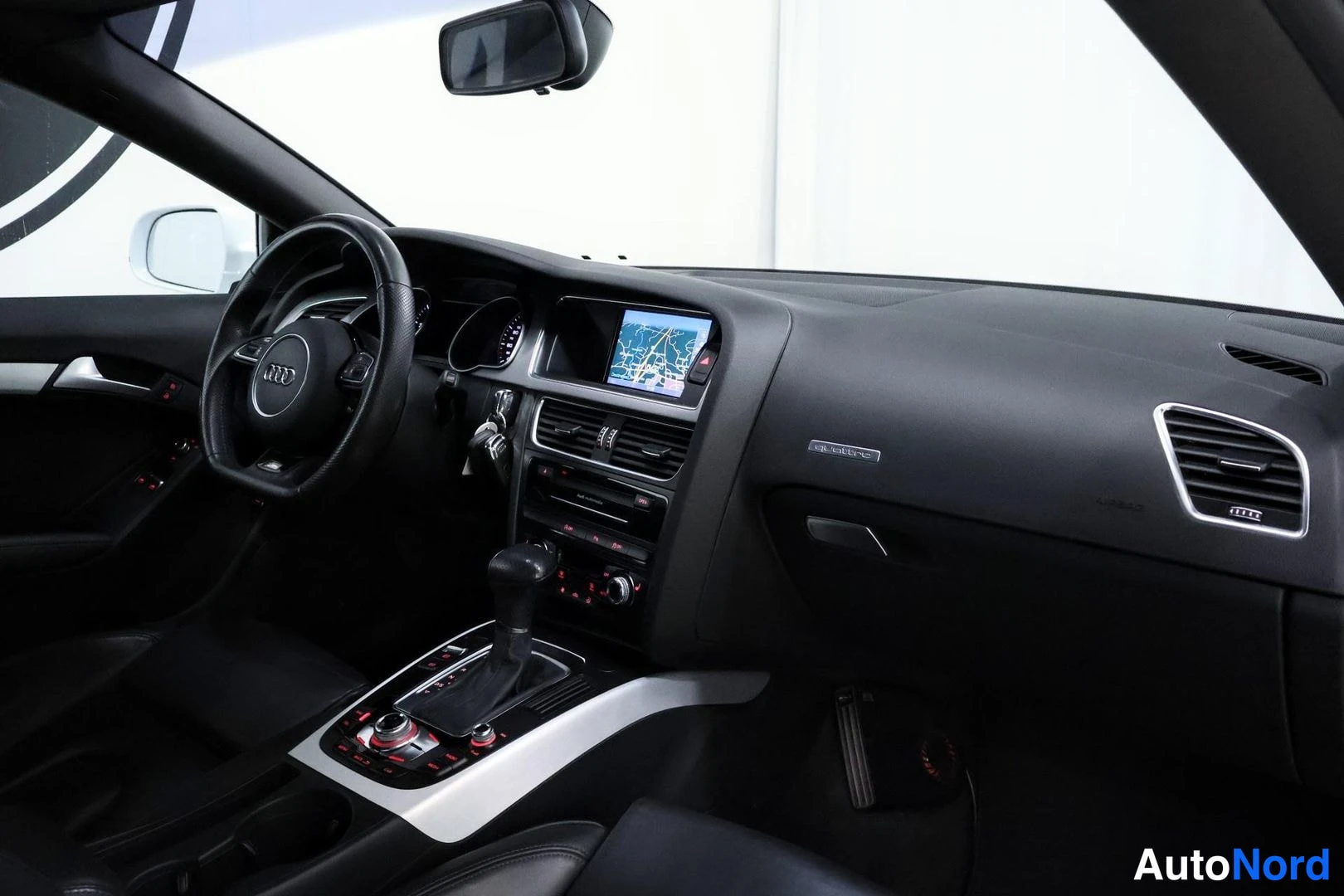 Ohjaamo: Full view of the dashboard extending across the front, showing the steering wheel, central infotainment screen displaying a map, climate control vents, and silv