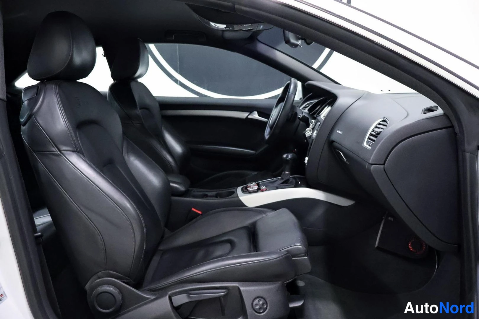 Etuistuimet: Interior view of the front cabin showing black leather driver and front passenger seats with multi-way adjustment controls visible on the side bolsters. Dashboa