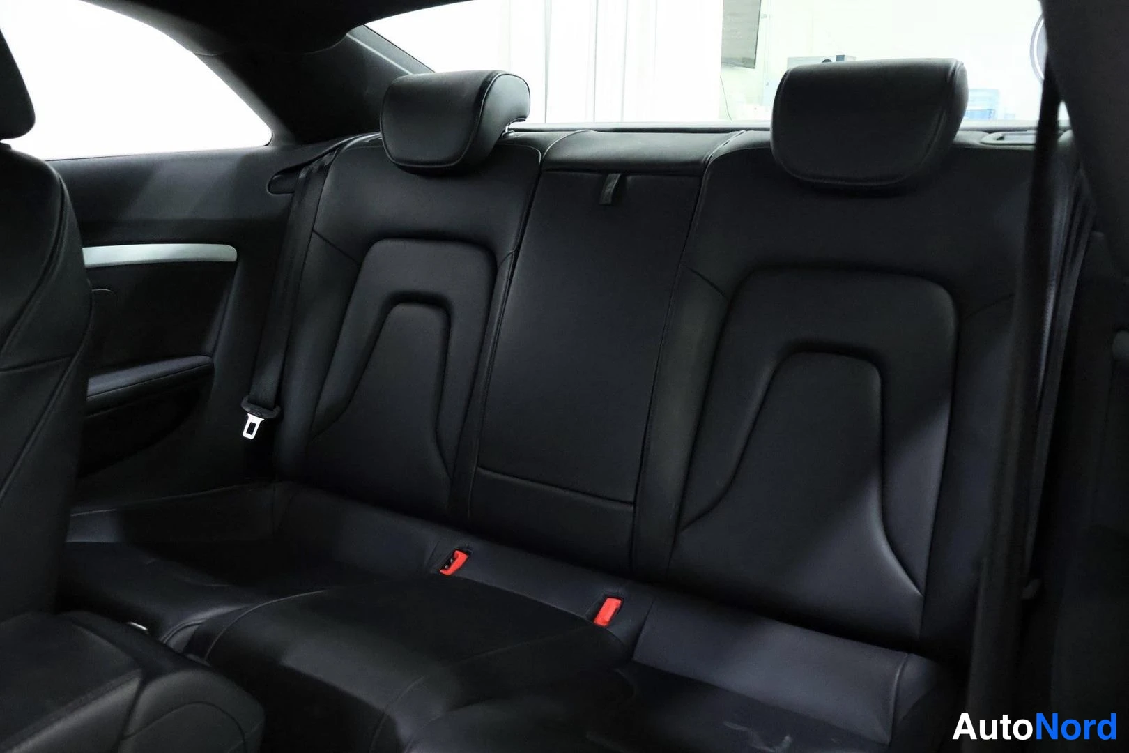 Takaistuimet: Rear bench seating area containing two rear headrests and three seatbelt buckles with red releases, set against a dark interior panel background.