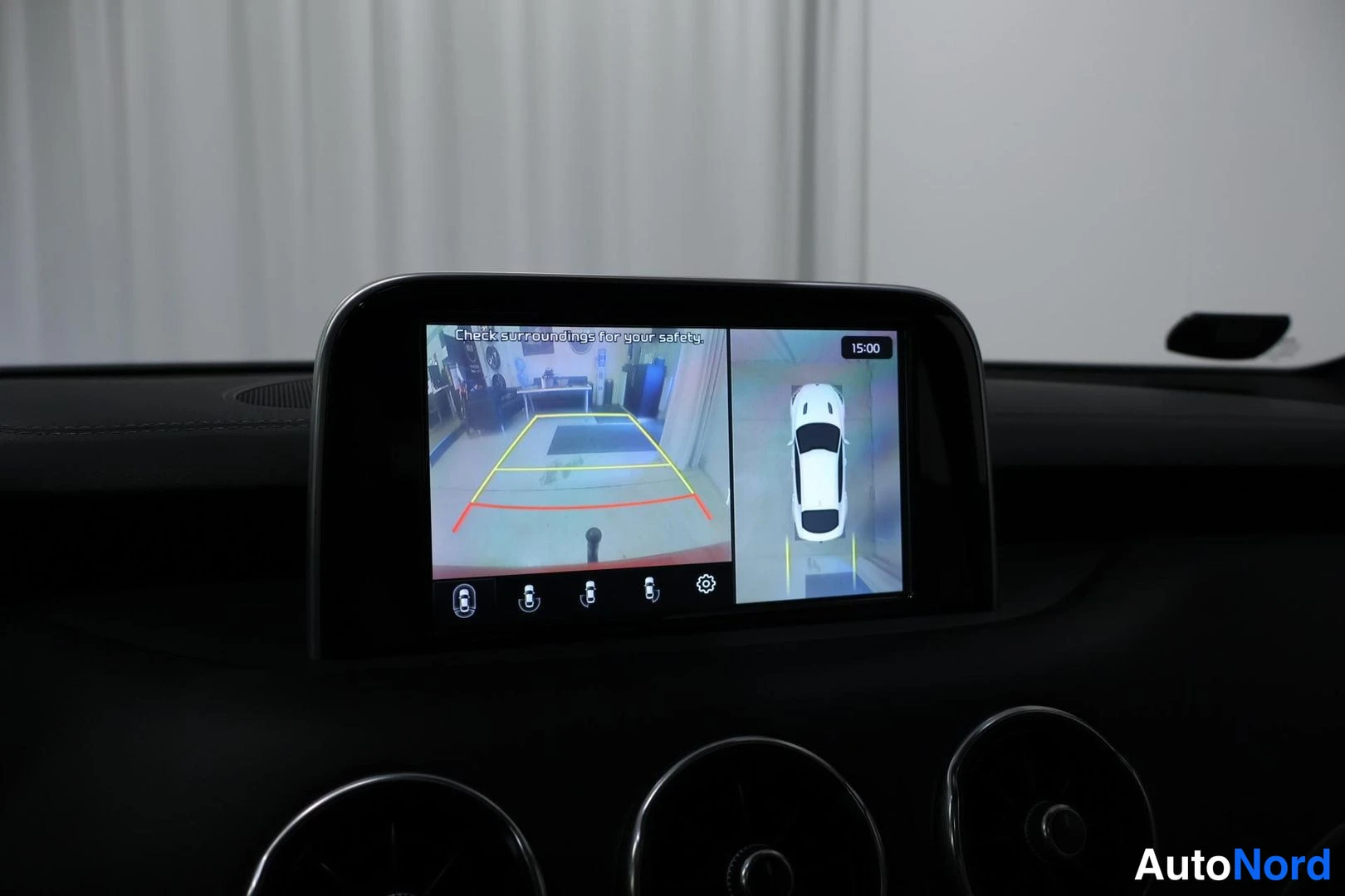 Edestä: Keskinäyttö näyttää peruutuskameran kuvan ohjausviivoineen ja 360-näkymän valkoisesta autosta ylhäältä