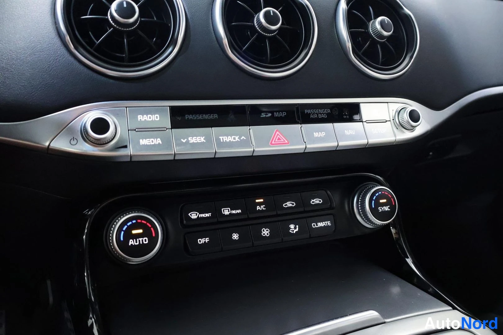 Yksityiskohta: Close-up of centre console climate controls: silver panel above houses RADIO, MEDIA and hazard warning buttons; lower black panel features dual temperature knob
