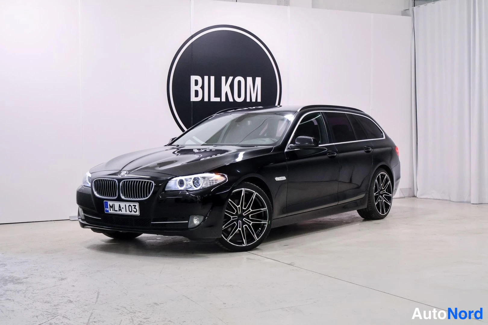 Etuviisto, nokka vasemmalle: Musta BMW 520 -farmari etukulmakuvassa, nenä vasemmalla; etusäleikkö, ajovalot, mustat kevytmetallivanteet ja rekisteritunnus näkyvät valkoista BILKOM-