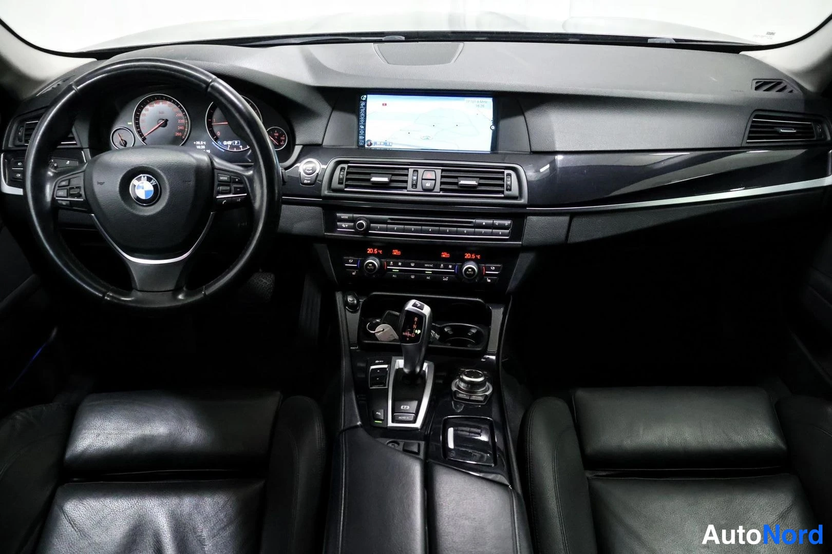 Etuistuimet: Full dashboard view of a BMW with black leather seats. A navigation screen is active in the center stack, flanked by climate controls and an automatic gear sele