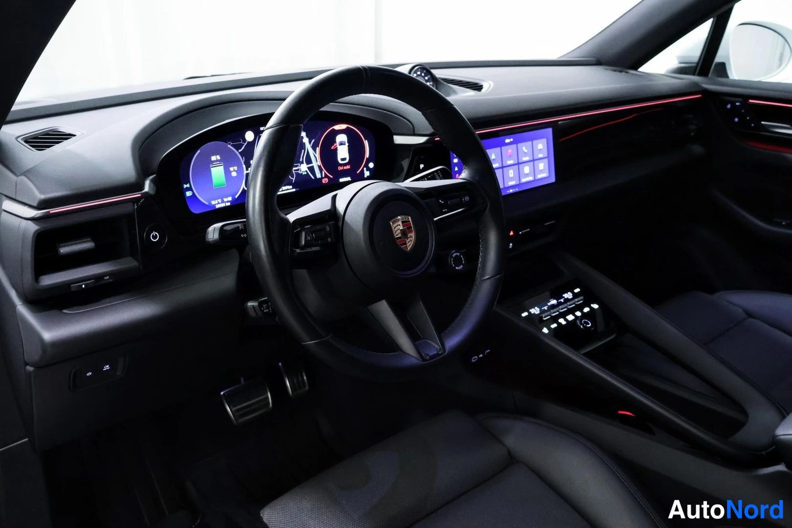 Sivulta: Sisätilakuva mustasta Porsche-ohjaamosta: merkkihallinta varustettu ohjauspyörä, digitaalinen mittaristo ja keskikonsolin kosketusnäyttö.