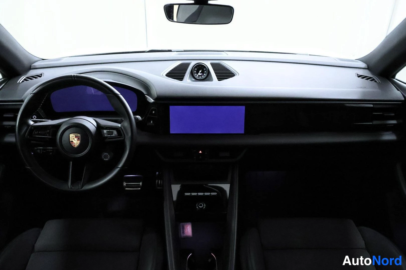 Etuistuimet: Interior view of a vehicle's dashboard featuring a multi-function steering wheel with the Porsche logo, two display screens (digital instrument cluster and info