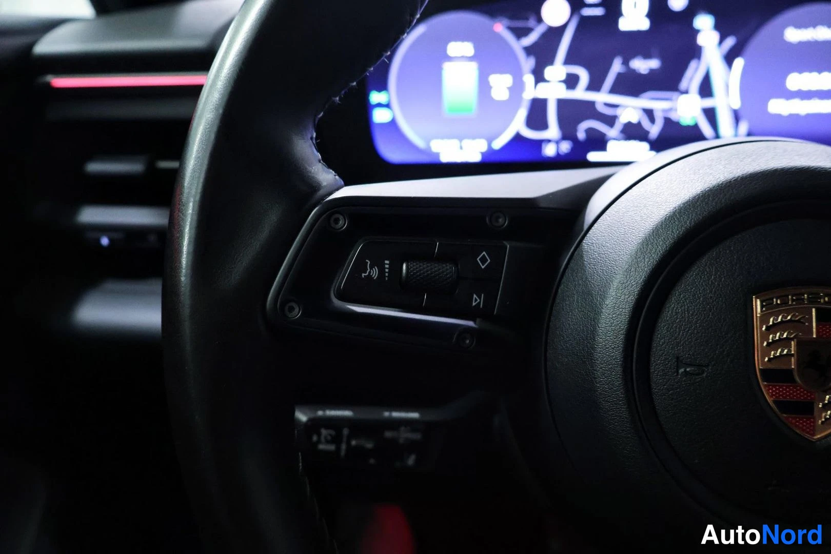 Yksityiskohta: Close-up of the left side of a black leather-wrapped steering wheel with control buttons for media and phone functions visible in the center hub area.
