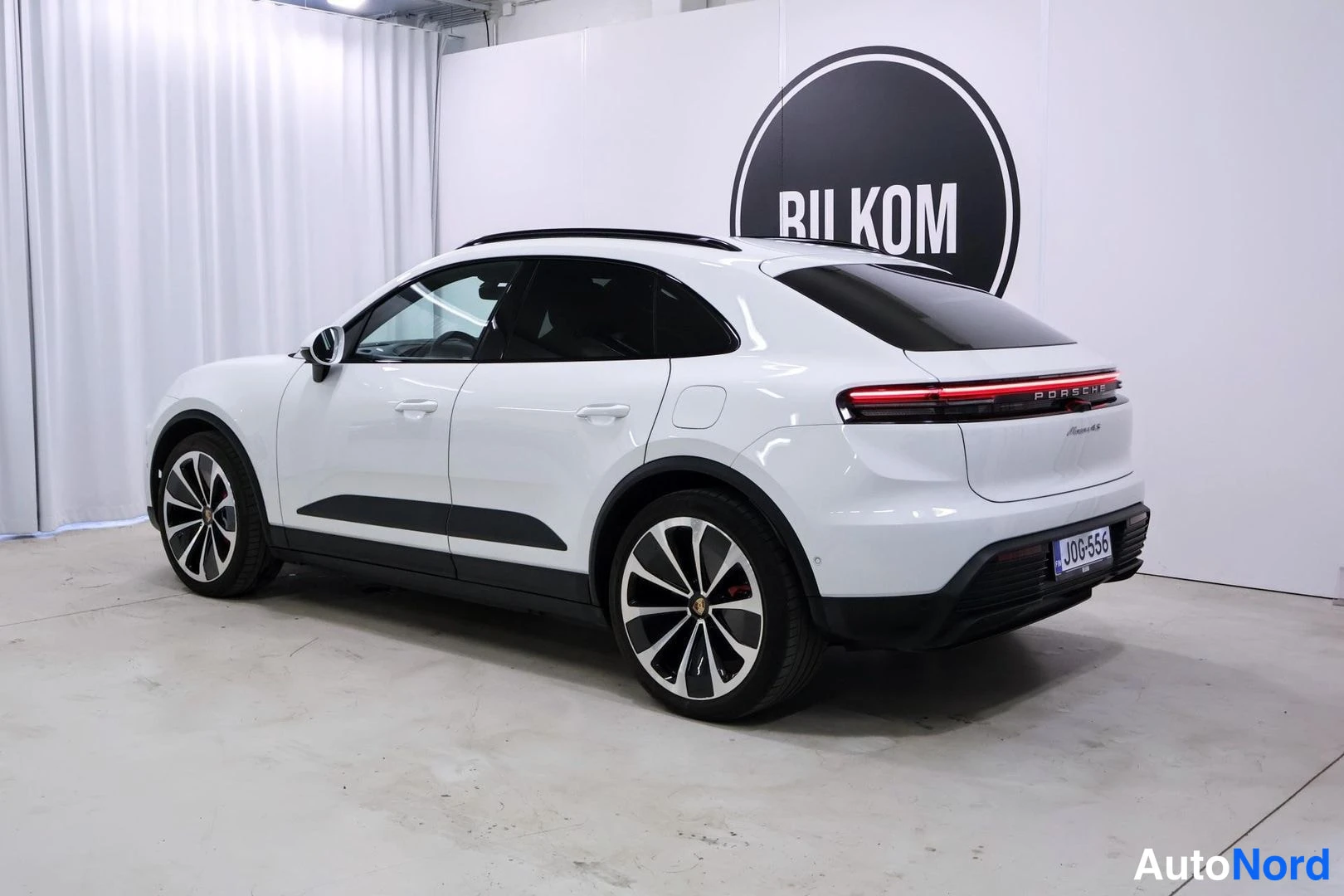 Takaviisto: Valkoinen Porsche Macan kolmeneljäsosan takanäkymässä, perä ja vasen kylki näkyvissä, rekisteritunnus, BILKOM-logo taustalla.
