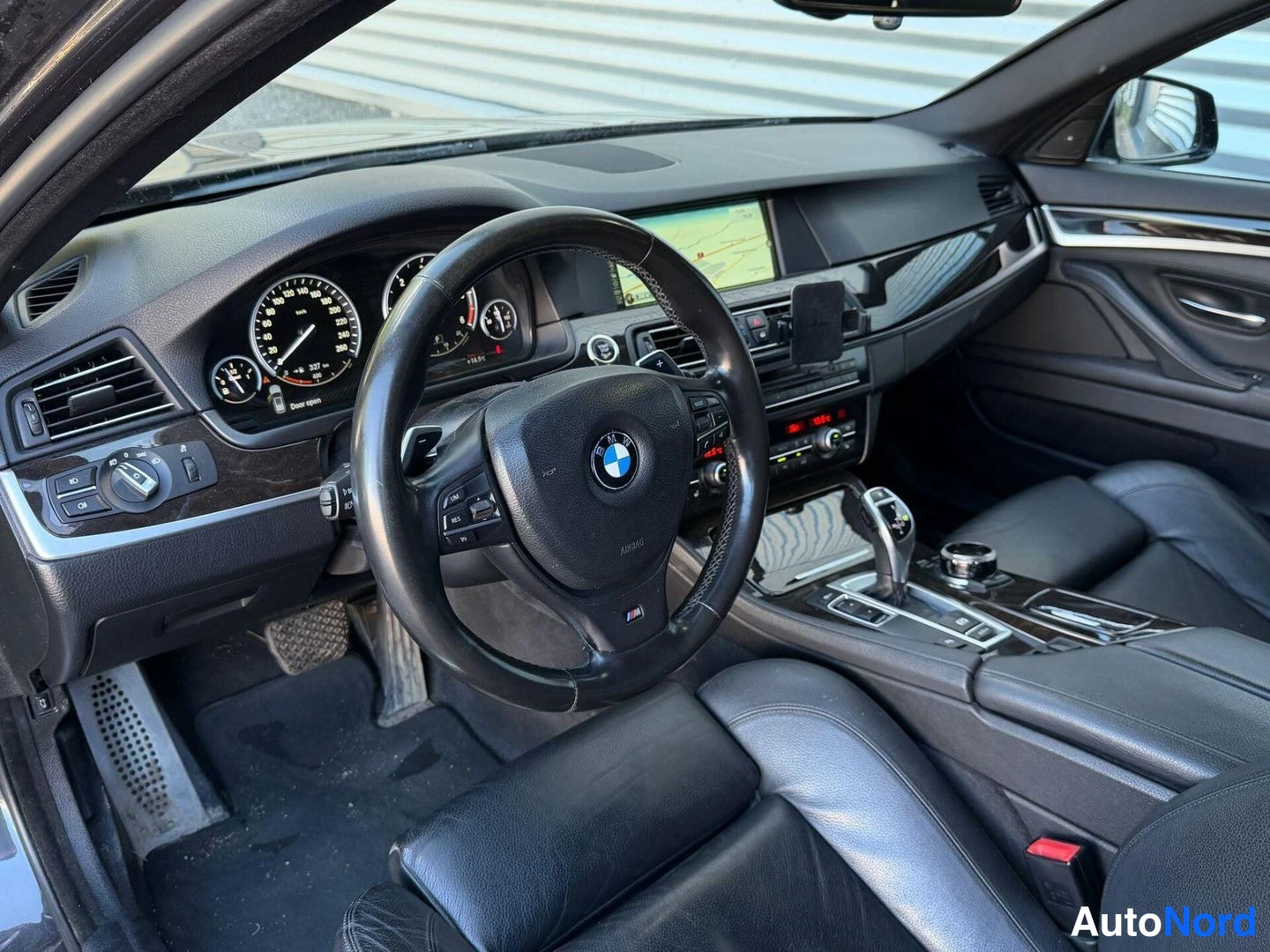 Muu: Ohjaamon sisäkuva: BMW-ohjauspyörä, analogiset mittarit ja keskikonsolin näyttö karttanäkymällä.