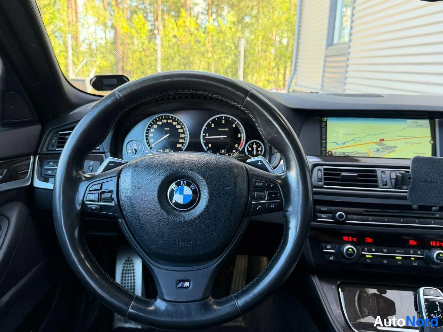 Muu: Ohjauspyörän lähi kuva, BMW-logo ja mittarit näkyvät taustalla karttana.
