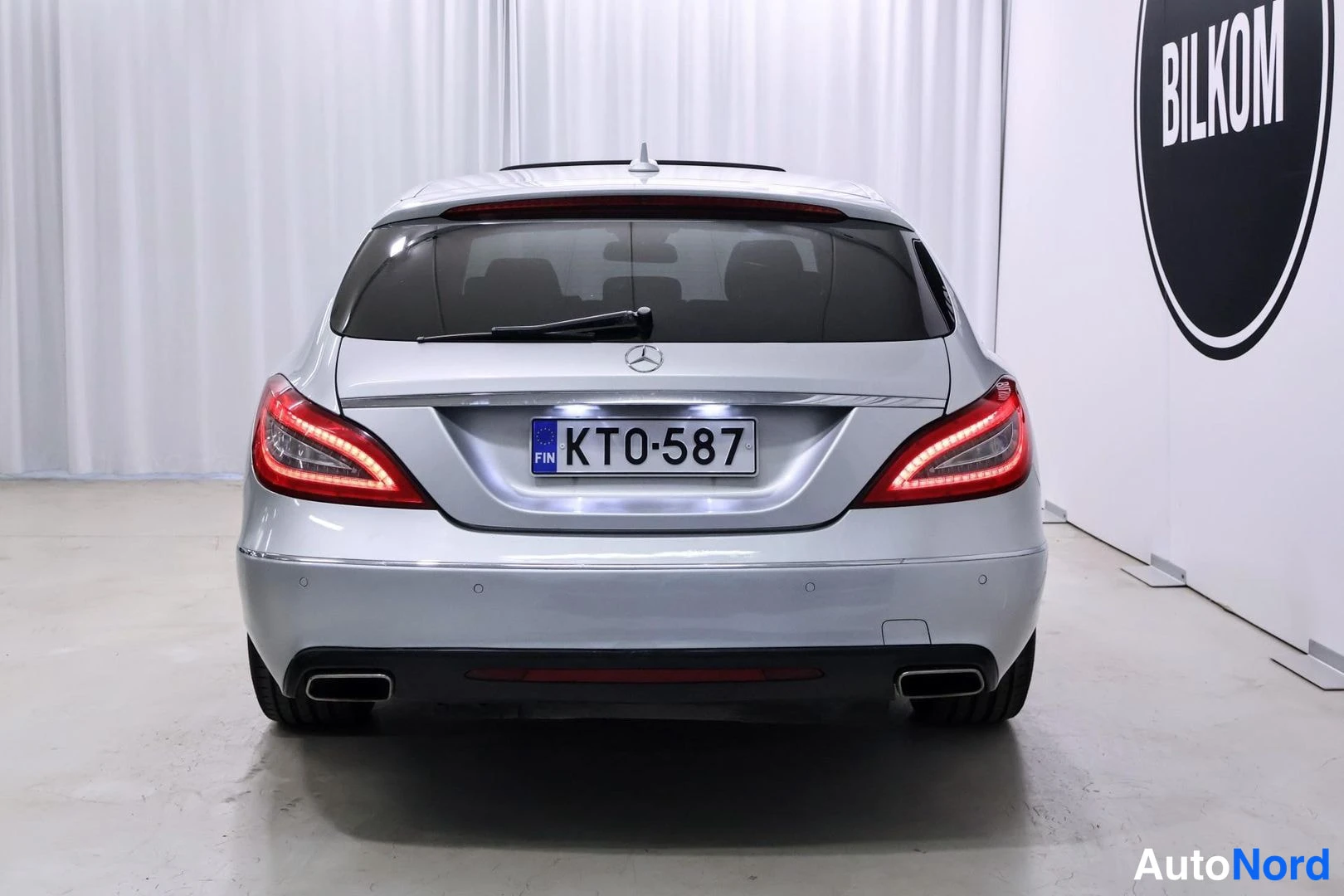 Takaa: Hopeisen Mercedes-Benz CLS -farmarin takapää suoraan takaa, rekisterikilpi KT0-587, BILKOM-tunnuksen vieressä.
