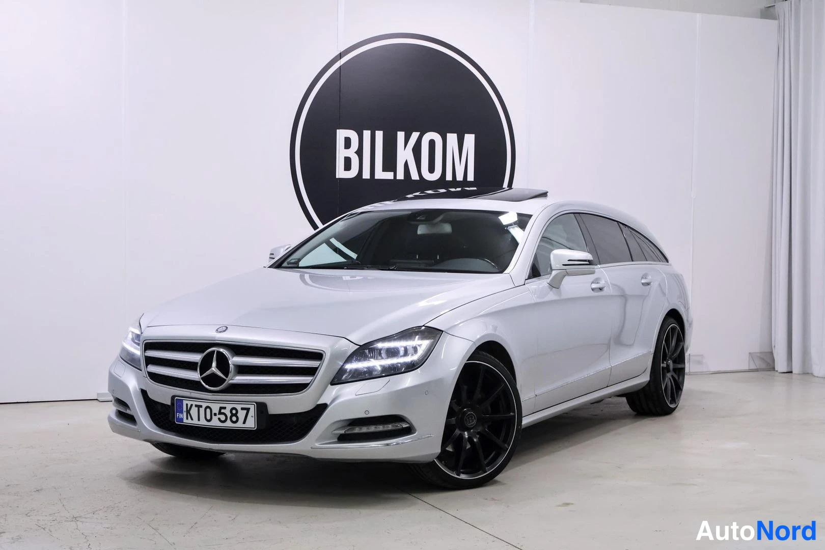 Etuviisto, nokka vasemmalle: Hopeinen Mercedes-Benz CLS -farmari kuvattuna etuokolokulmasta niin, että keula osoittaa kuvan vasempaan reunaan. Etusäleikkö ja Mercedes-tähti sekä aj