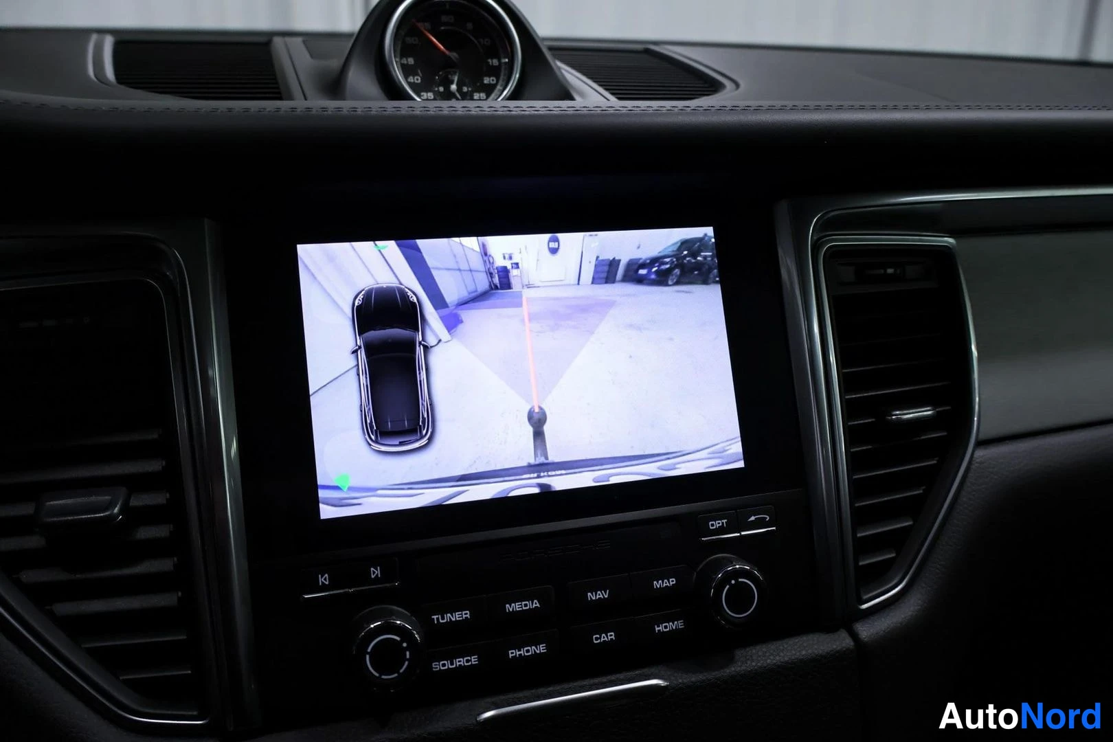 Muu: Kosketusnäyttö, jolla näkyy peruutuskameran kuva: mustan auton katse ylhäältä ja apuviivat pysäköintihalliin; alla TUNER/MEDIA/NAV/MAP/SOURCE/PHONE/CAR/HOME-nap