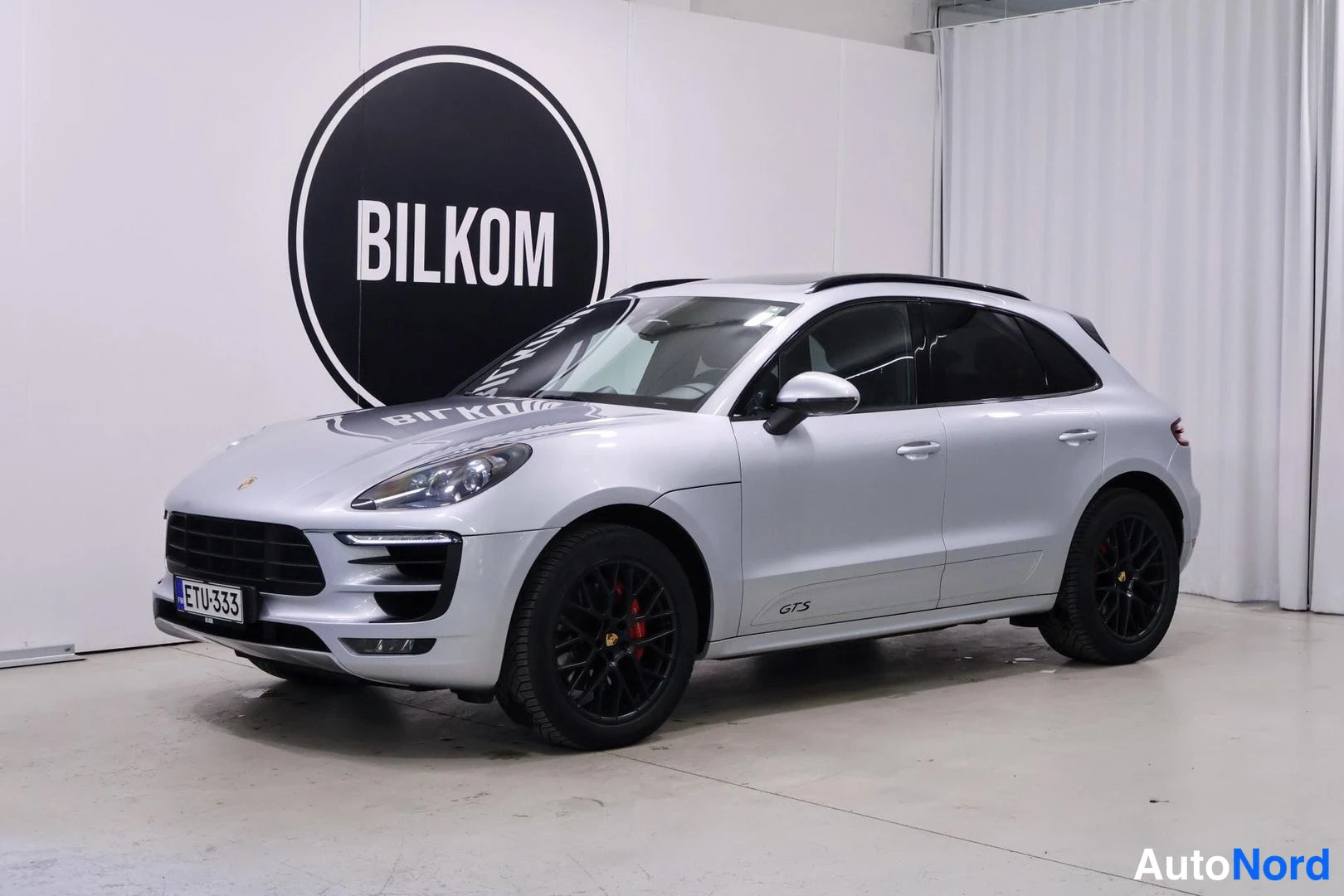 Etuviisto, nokka vasemmalle: Vasen kolmas näkökulma: Valkoinen Porsche Macan GTS, mustat vanteet ja katotelineet. Taka-ikkunoiden takana tumma sisätila.