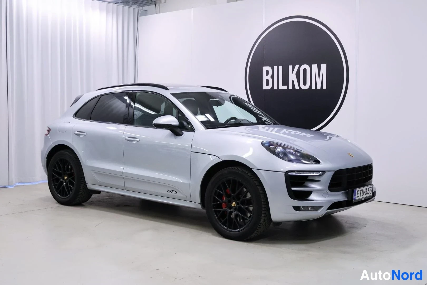 Etuviisto, nokka oikealle: Hopeanharmaa Porsche Macan GTS-nelivetoisen urheilumaastopyörän etukulmakuvassa, mustat vanteet ja punaiset jarrusatulat.