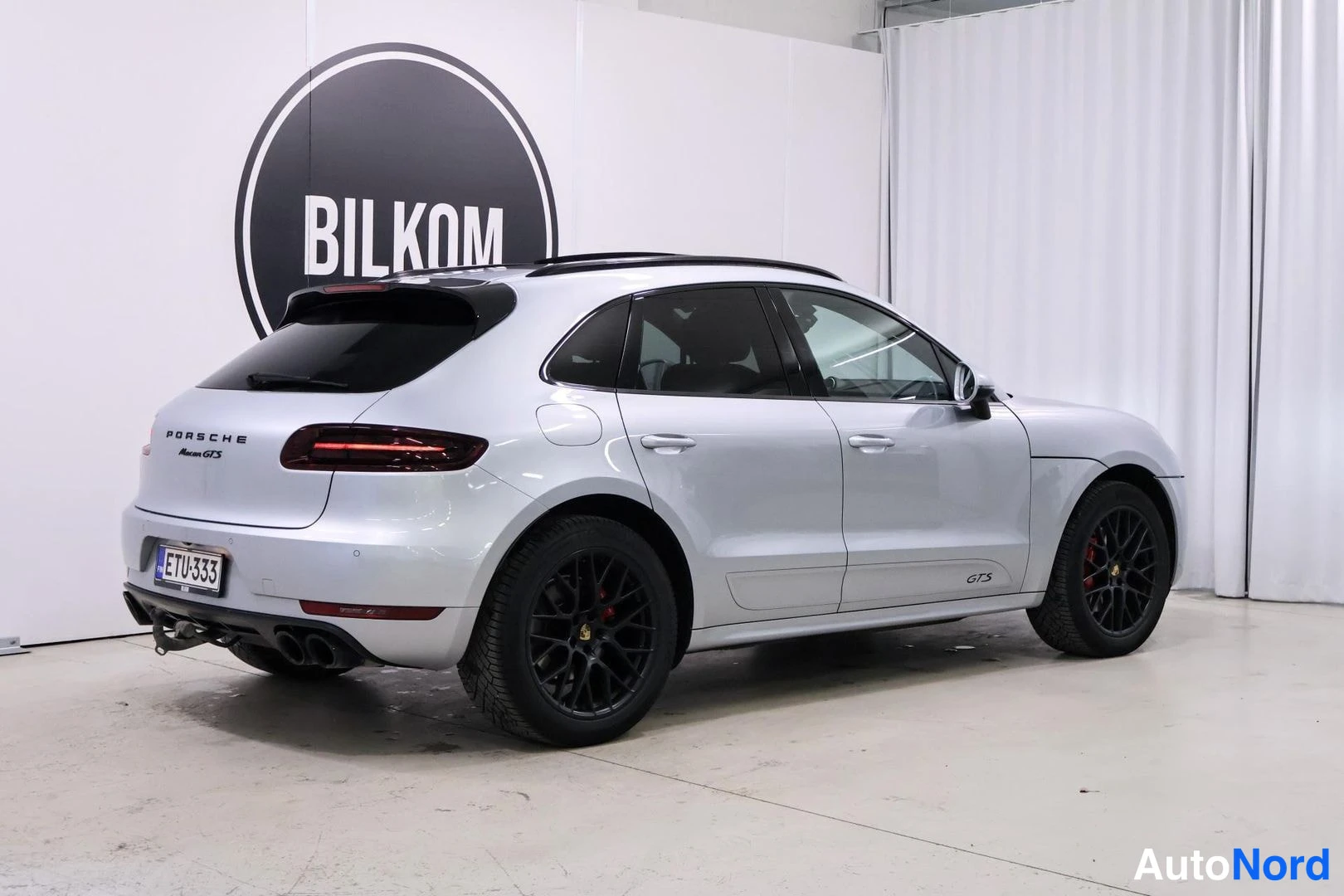 Takaviisto: Hopeanvärinen Porsche Macan GTS takaviistosta valokuvattuna studiossa, tummat astinaluvet.