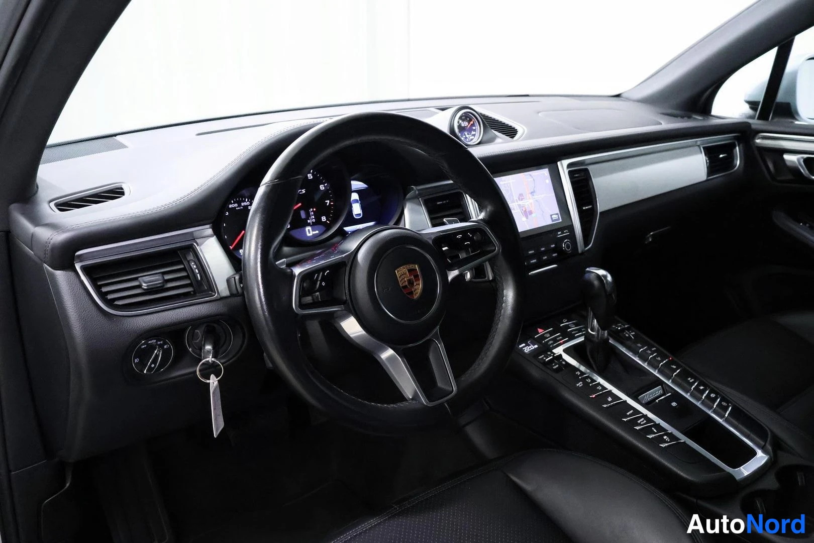 Muu: Ohjaamosta vasemmanpuoleinen näkymä: Porsche-ohjauspyörä, mittaristo, kosketusnäyttö ja vaihteenvalitsin, avain sytytyslukossa.