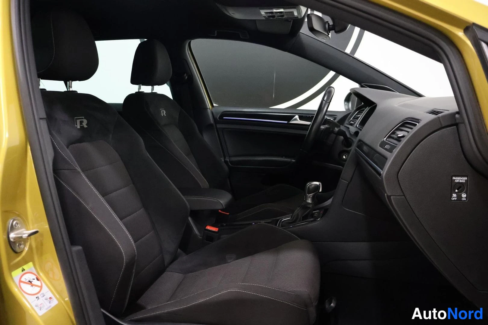 Etuistuimet: Interior shot showing two front sport seats and dashboard. Dashboard features air vent and glovebox area. Yellow exterior door frame visible.