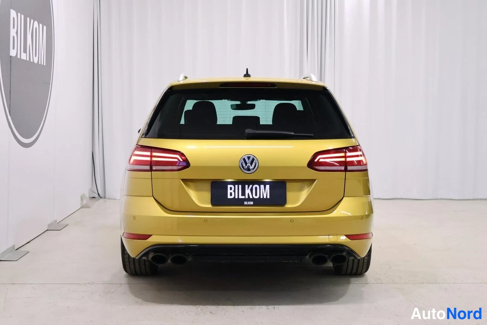 Takaa: Keltaisen farmariauton suora takanäkymä, näkyvissä takavalot, VOLKSWAGEN-merkki, BILKOM-näyttömärkki ja neljä pakoputkea.