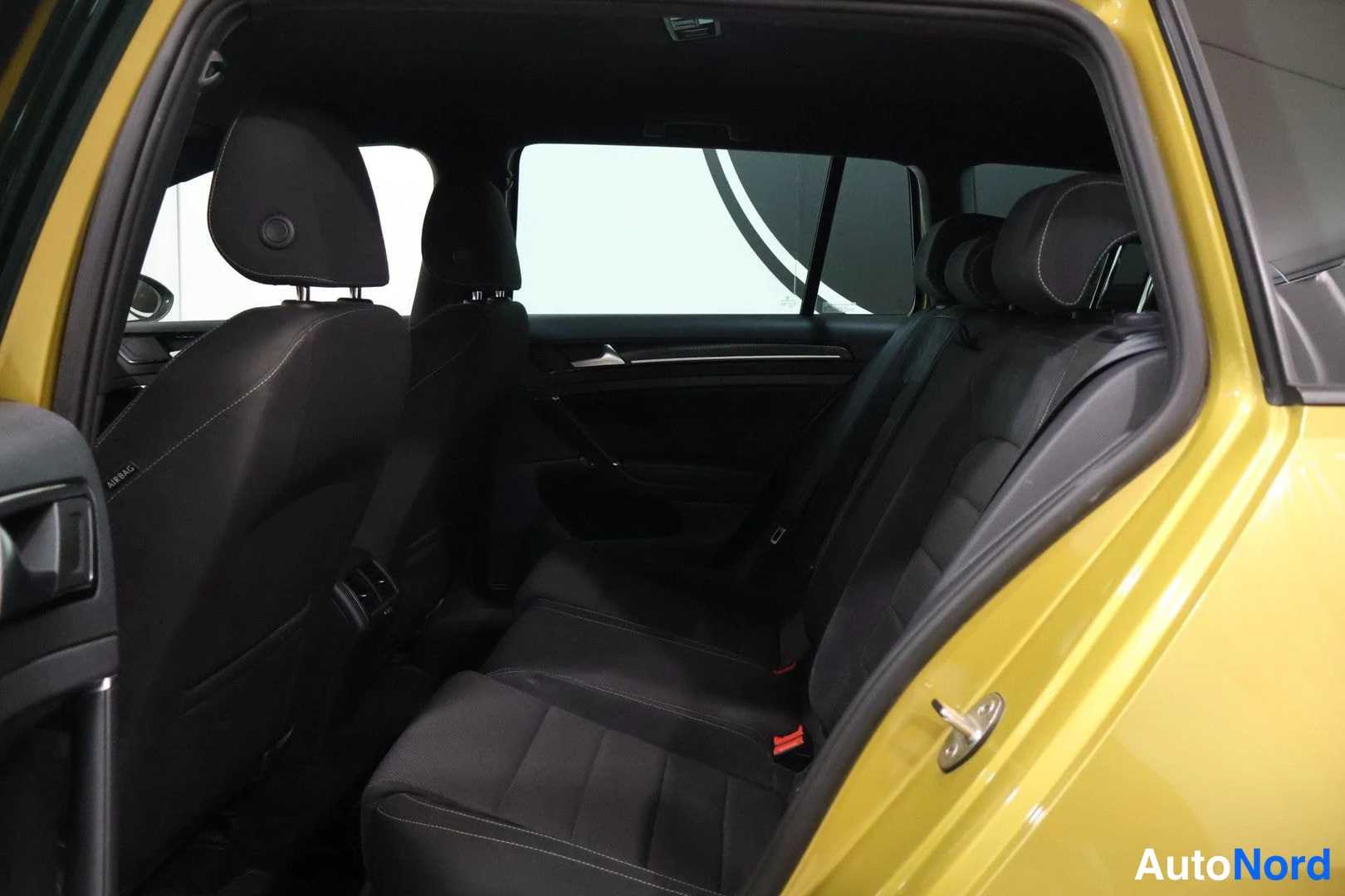 Takaistuimet: Interior rear cabin view showing back bench seat and side windows through open right rear door. Yellow door frame in foreground.