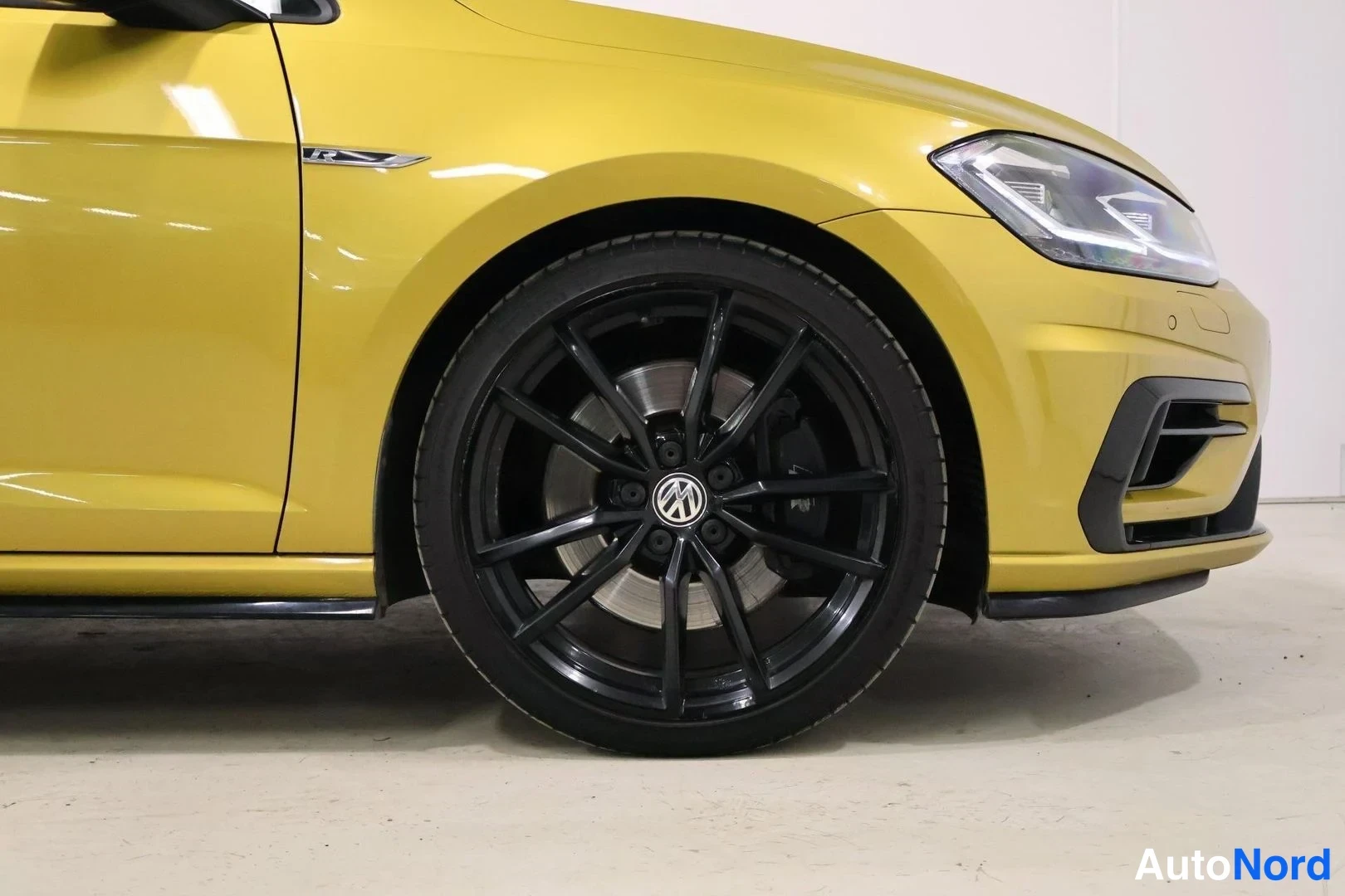 Etuviisto, nokka oikealle: Keltainen Volkswagen Golf, etukulma; musta kevytmetallivanne ja VW-merkki näkyvät etupyörän yhteydessä.