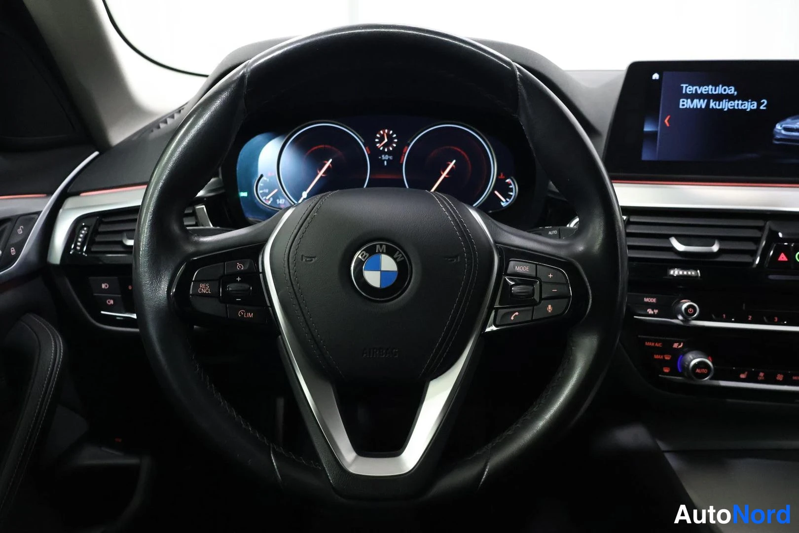 Muu: Ohjauspyörä ja kojelauta: BMW-merkitty ohjauspyörä, digitaalinen mittaristo ja infotainment-näyttö jossa teksti 'Tervetuloa, BMW kuljettaja 2'.